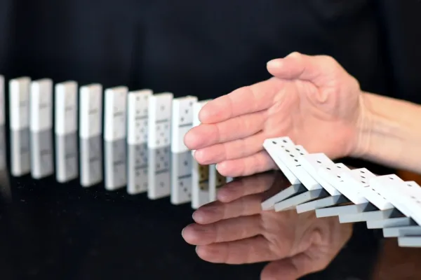 Hand hält umfallende Dominosteine auf